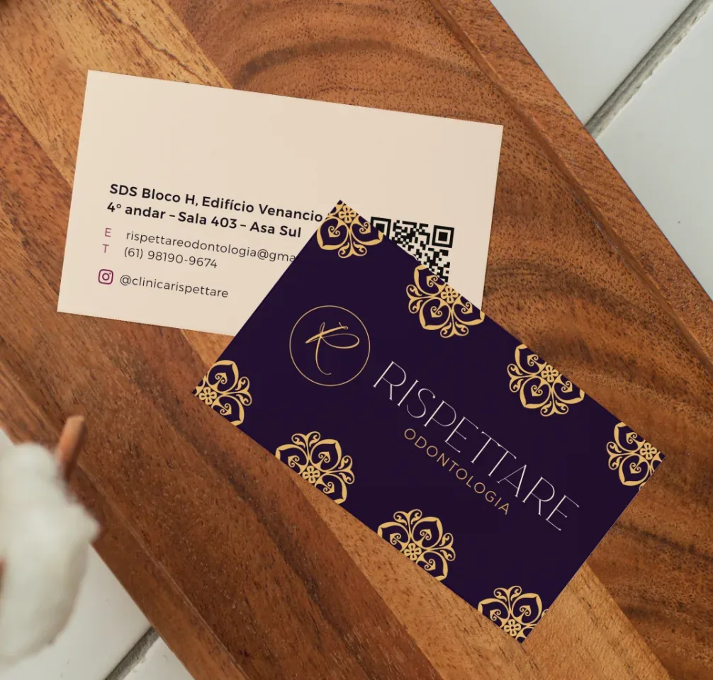 Dois cartões de visita da Clínica Rispettare sobre uma tábua de madeira: um com o logotipo dourado sobre fundo roxo, o outro com os dados de contato.